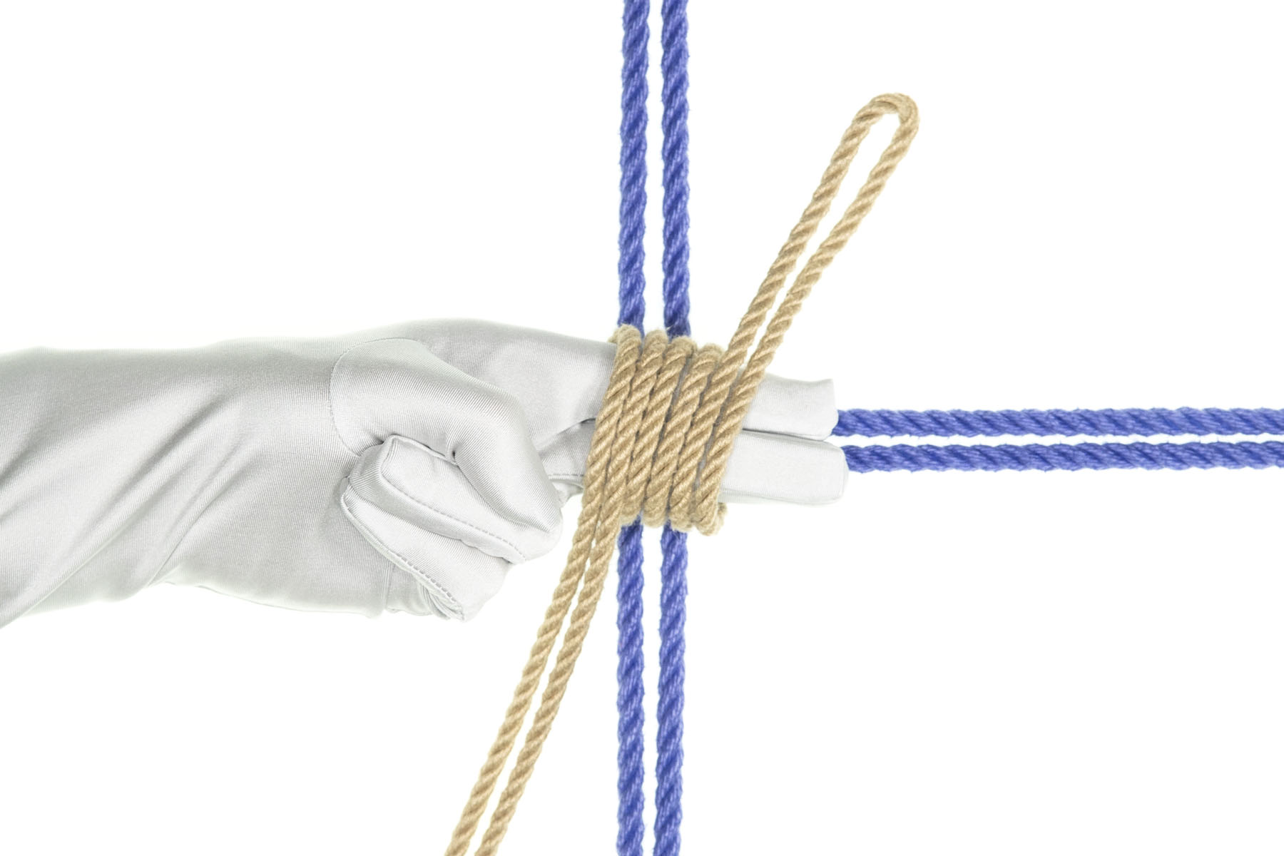 A left hand in a white glove is laid on top of the horizontal blue rope, crossing over the intersection with the vertical blue rope. The index and middle fingers are extended along the blue rope to the right of the image and the ring and pinkie fingers are folded. The tan rope has been collapsed into a tight spiral wrap around the index and middle fingers.