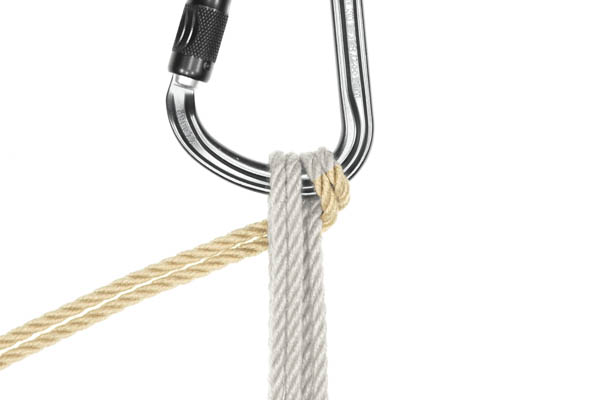 The second pass of the rope has been pulled to the left of the image, passing behind itself and the first pass. As it passes over the carabiner, it is now held snugly in place between the carabiner and the rope descending from the back of the carabiner.